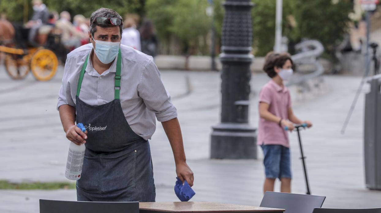 Un camarero limpia una mesa de un bar en Sevilla con un desinfectante