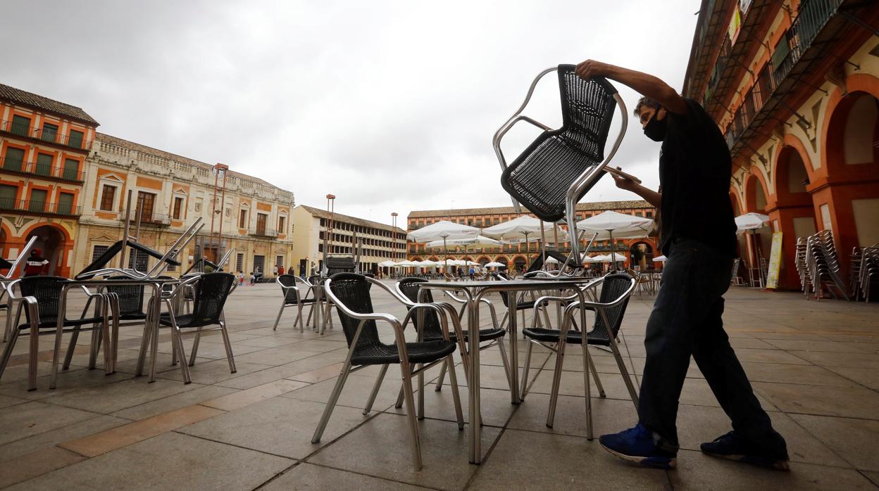 Un camarero recoge las sillas de su terraza en una plaza de la Corredera desierta