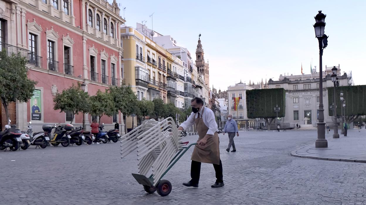 Un hostelero recoge el mobiliario de la terraza de un bar de Sevilla