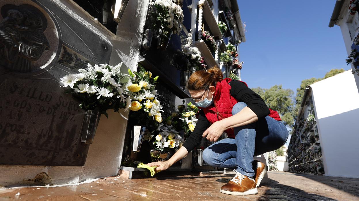 Una mujer con mascarilla limpia un nicho en el cementerio de San Rafael