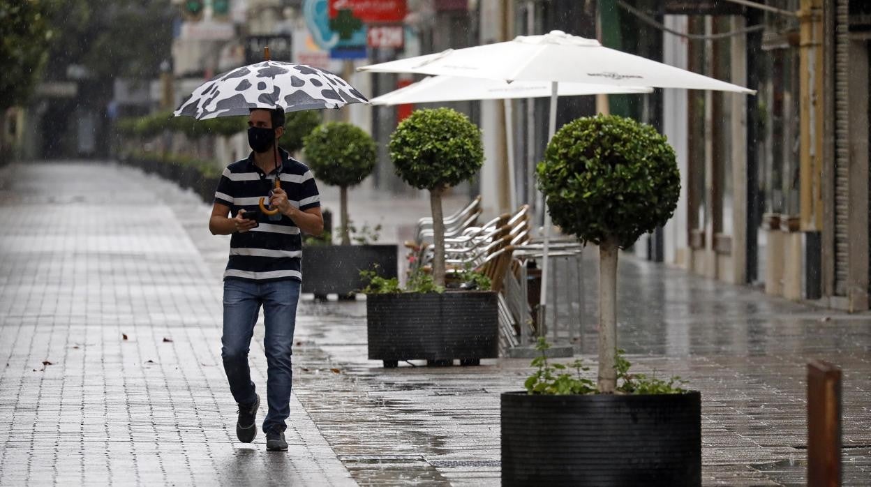 Un hombre pasea bajo la lluvida por la calle Cruz Conde de Córdoba