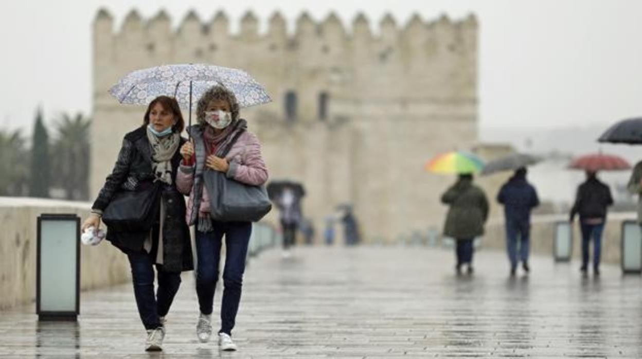 Dos mujeres se protegen de la lluvia mientras pasean por el Puente Romano