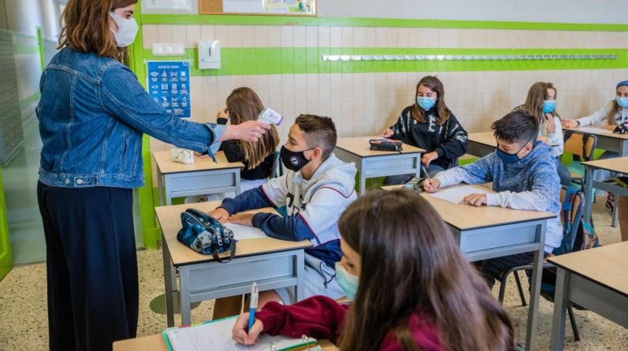 Una profesora toma la temperatura a un alumno en un aula