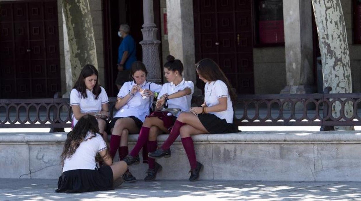 Un grupo de escolares se sienta en un banco sin uso de la mascarilla