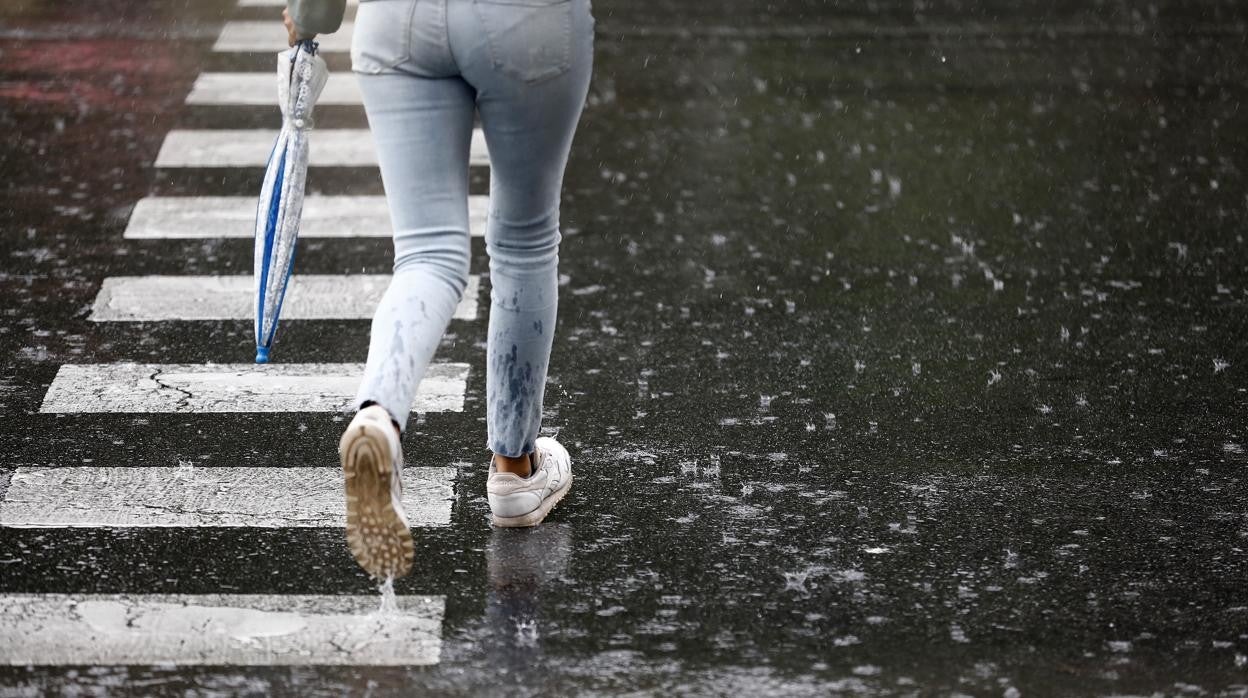 Una joven cruza un paso de peatones en un día lluvioso