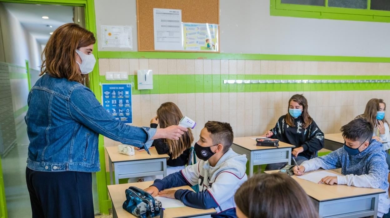 Una docente toma la temperatura a los niños en clase