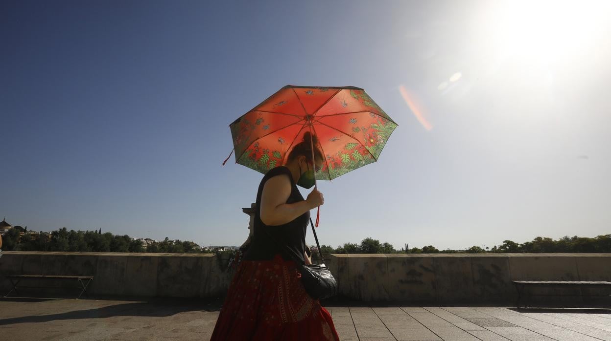 Una mujer cruza el Puente Romano de Córdoba este sábado bajo un paraguas para protegerse del sol