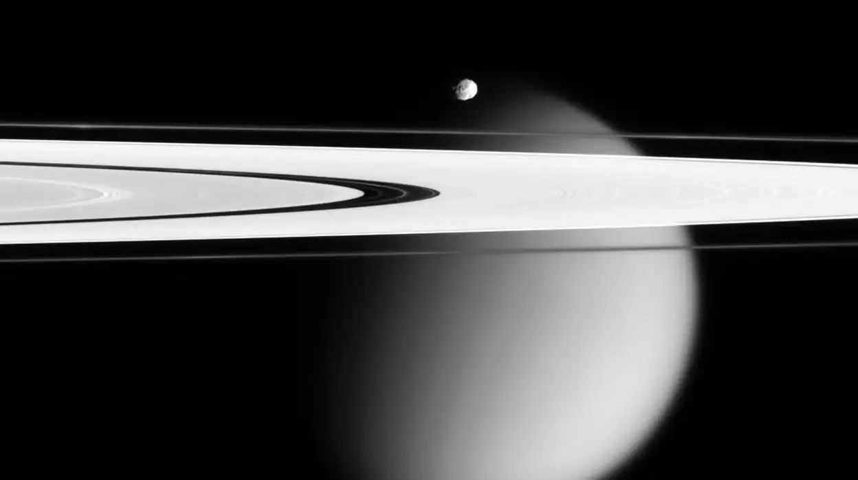Vista de Epimeteo, luna menor de Saturno, sobre los anillos. Al fondo, Titán