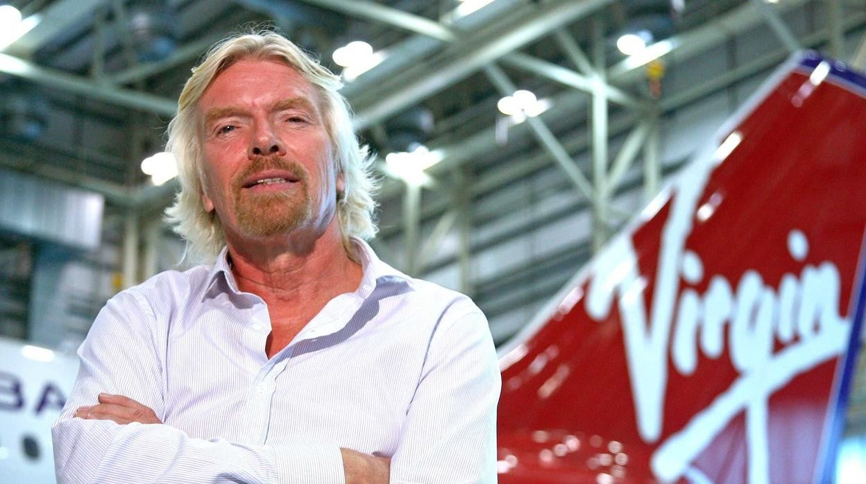 Richard Branson posando con una nave de su compañía espacial en segundo plano