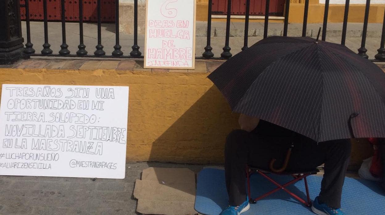 El novillero, cubierto bajo un paraguas, junto al cartel en el que exigía una novillada en San Miguel