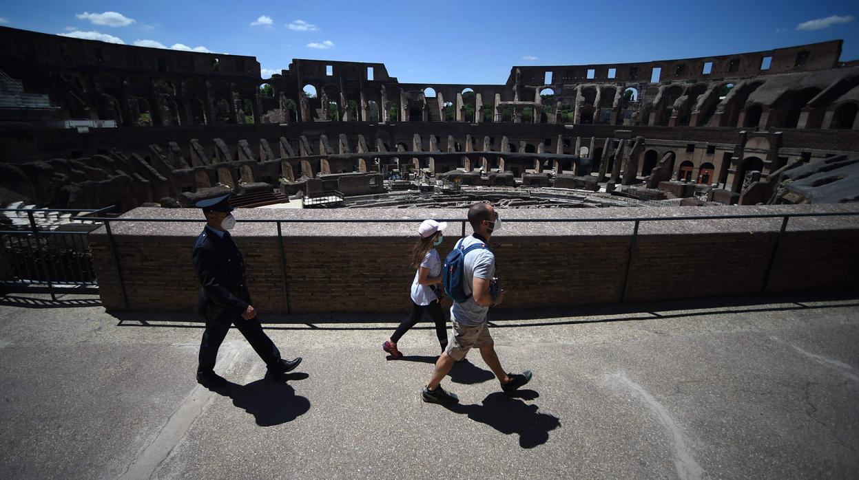 Unos turistas con mascarilla seguidos por un guarda de seguridad en el Coliseo de Roma