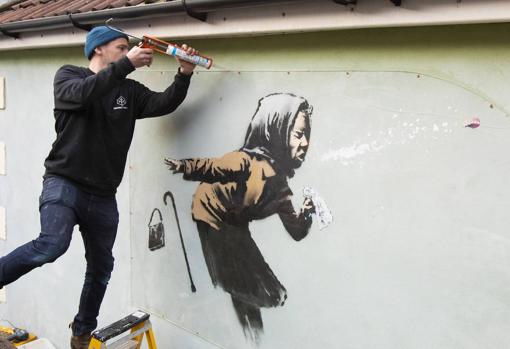 Fred Loosmore coloca una cubierta protectora de metacrilato sobre la nueva creación titulada '¡¡Aachoo !!' por el artista callejero británico Banksy