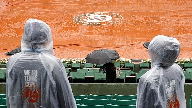 Aficionados con chubasqueros y paraguas en la joranda cancelada en Roland Garros