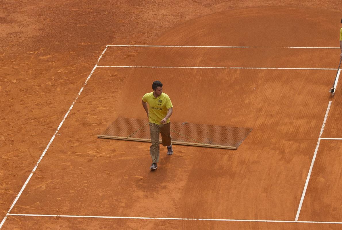Dos pisteros pasando la estera y limpiando las líneas tras un partido