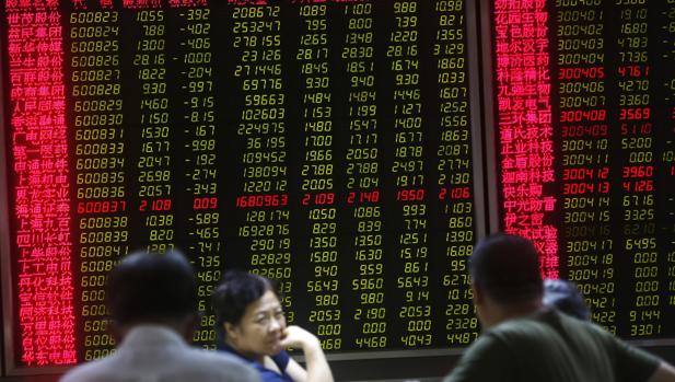 Varios inversores chinos sentados delante de las pantallas que muestran diversa información bursátil en una compañía de corretaje de Pekín (China)
