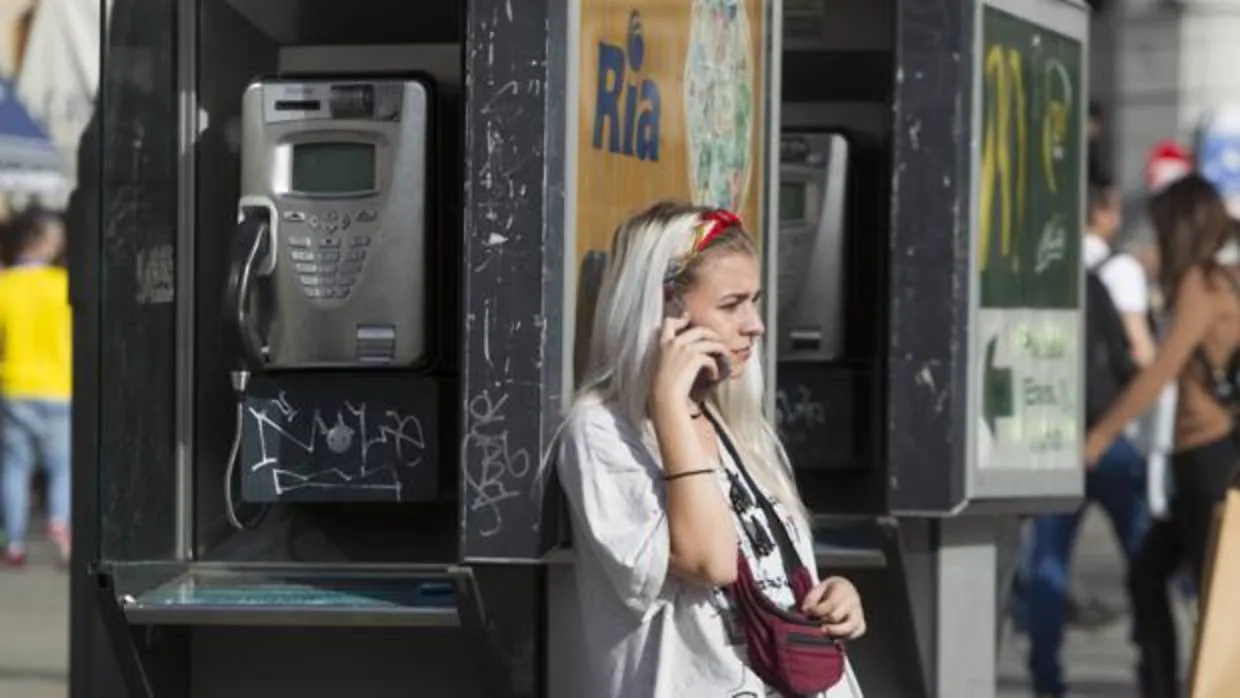 Una cabina de teléfono, en contraposición con una mujer que habla por su móvil