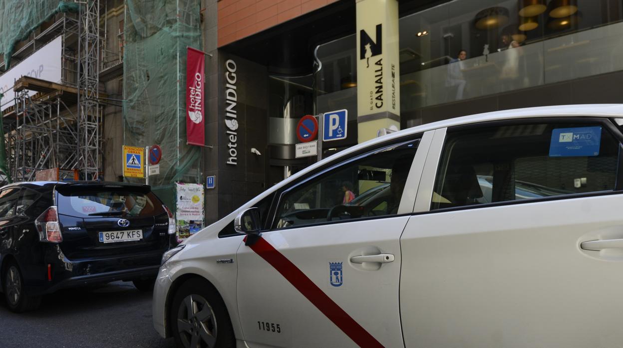 Un vehículo con licencia VTC y un taxi, frente al hotel Indigo en Madrid