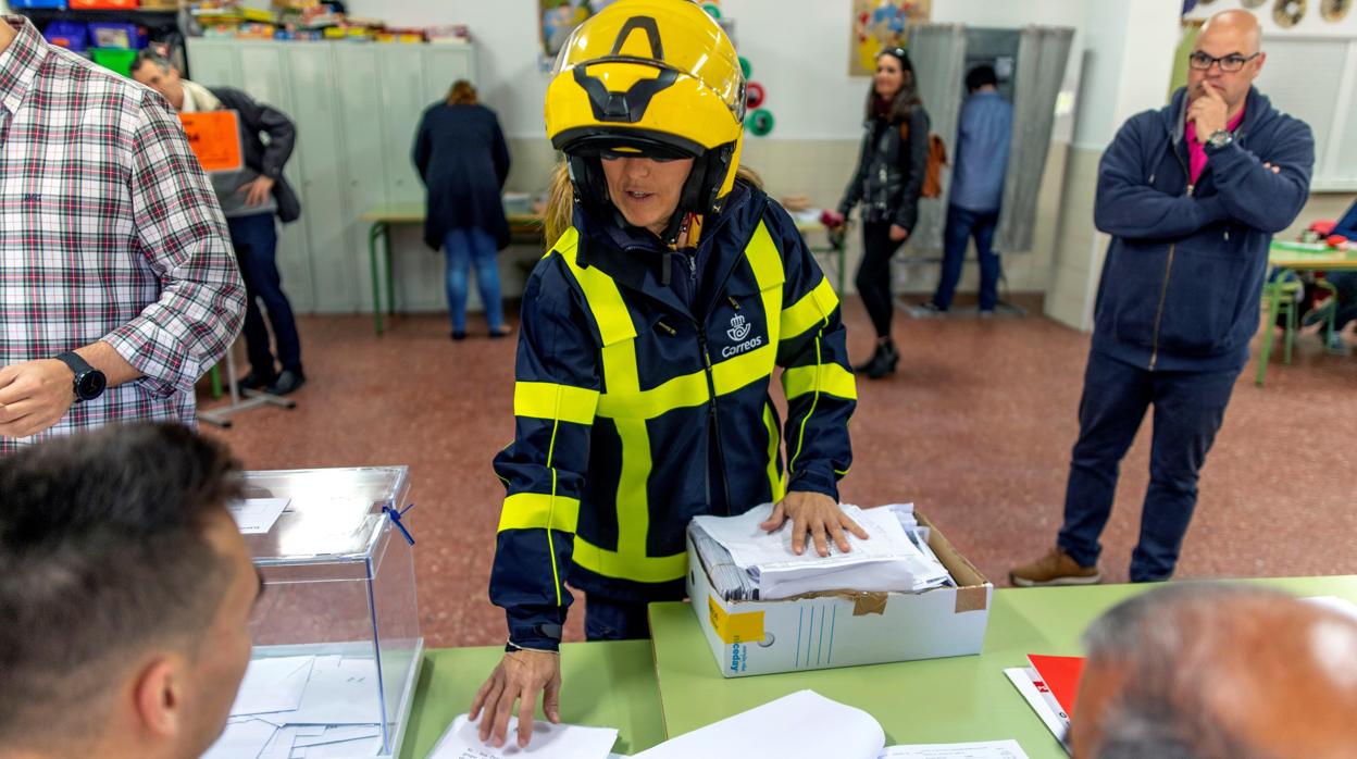 Una trabajadora postal de Correos entrega votos por corresos en la mesa de un colegio electoral de Toledo