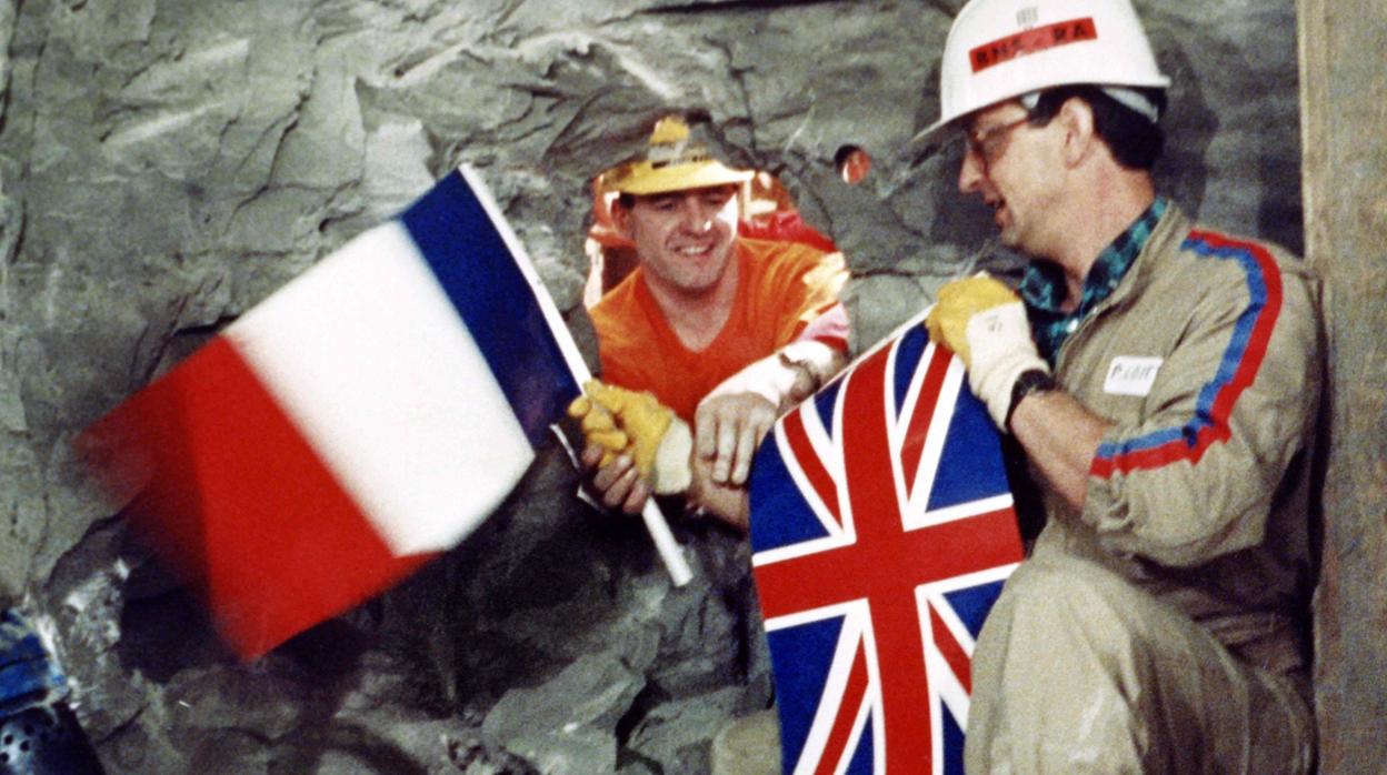 Los trabajadores del túnel Philippe Cozette de Francia y Graham Fagg de Reino Unido se dan la mano mientras sostienen banderas nacionales, durante el histórico avance que unía ambas partes, en 1990