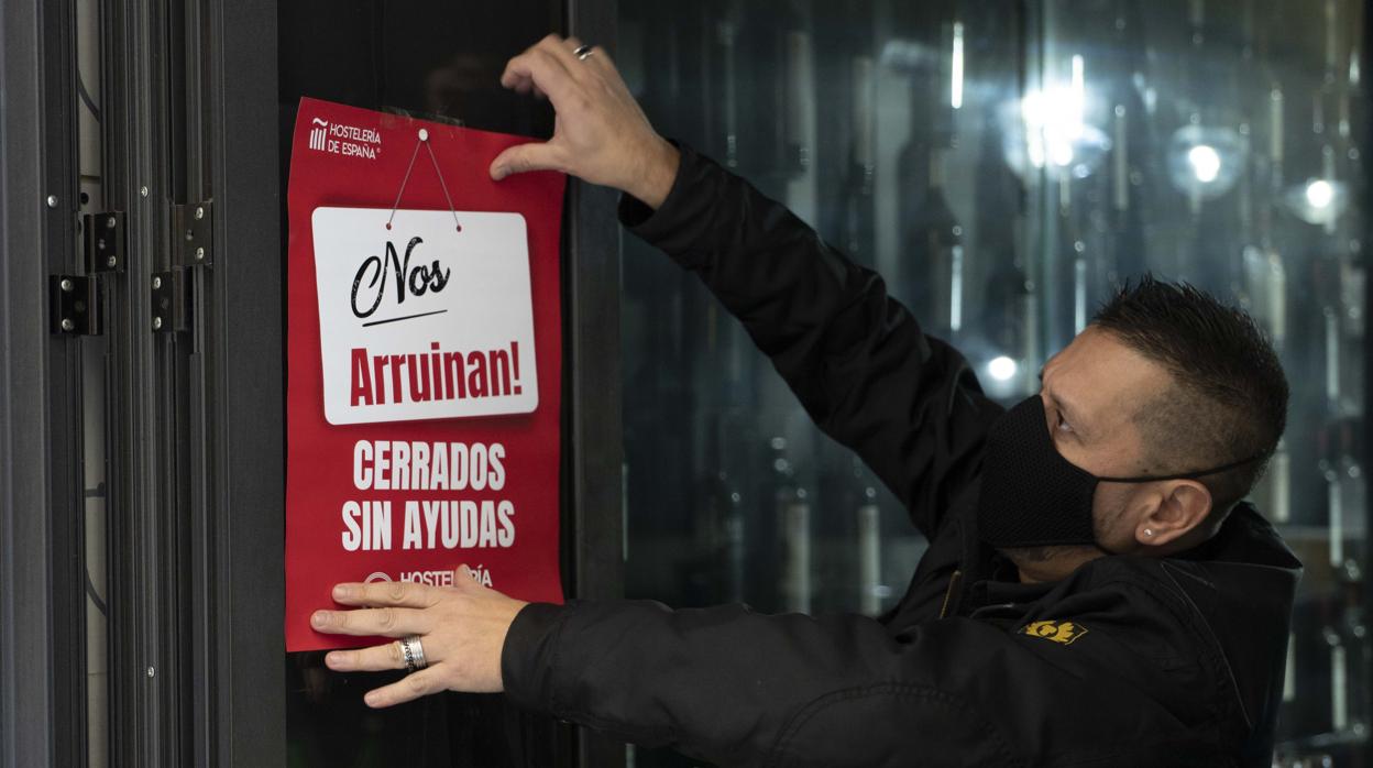 Un trabajador de hostelería coloca un cartel donde se lee «Nos arruinan. Cerrados sin ayudas»