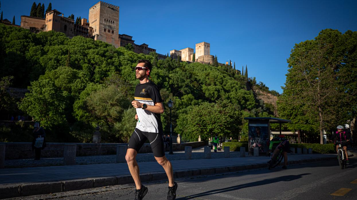 Un corredor hace deporte en el Paseo de los Tristes de Granada con la Alhambra al fondo