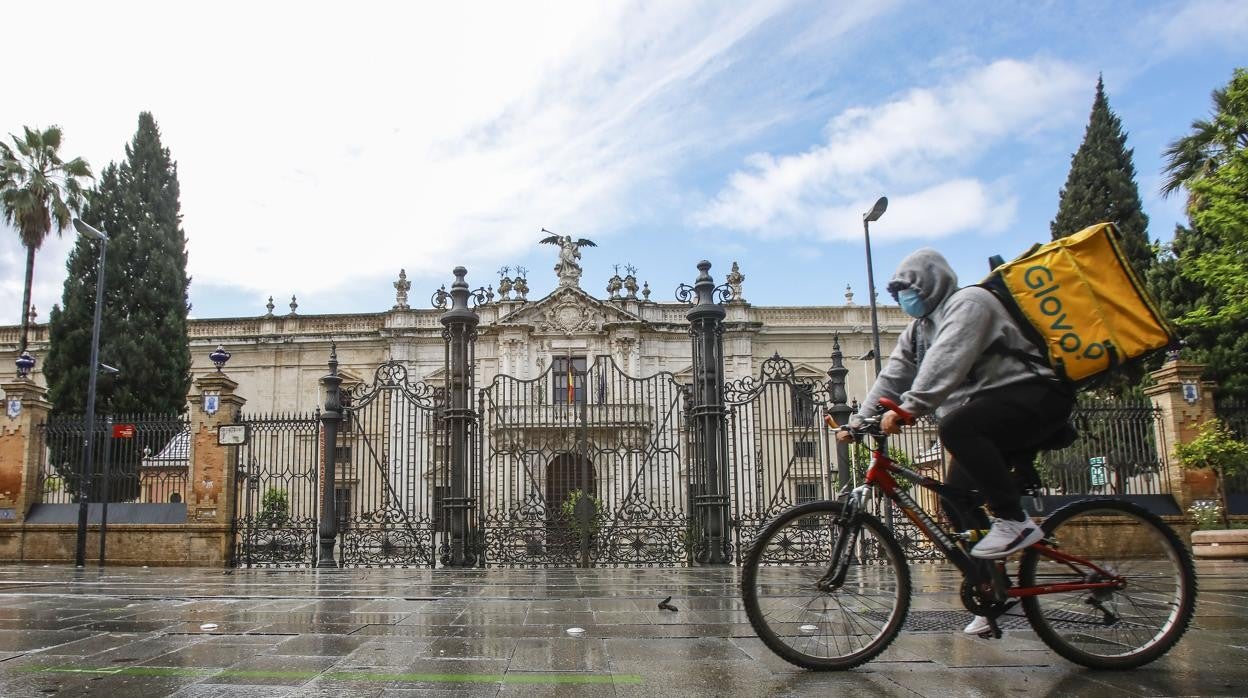 Un repartidor pasa en bicicleta por delante del rectorado de la Universidad Hispalense