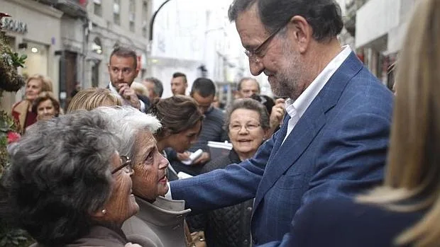 El presidente del Gobierno y candidato a la reelección por el PP, Mariano Rajoy, conversa con dos mujeres durante un paseo por Vigo