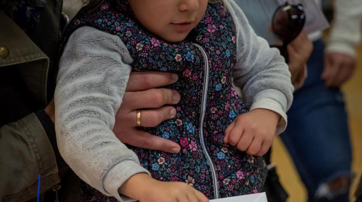 Un padre sostiene a su hija para que pueda introducir el sobre con el voto en una urna en el colegio público Alfares en el sevillano barrio de Triana en las Generales de 2019