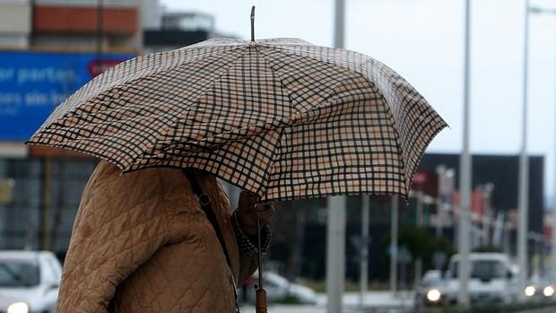 Una mujer se cobija del viento y la lluvia en Ponferrada