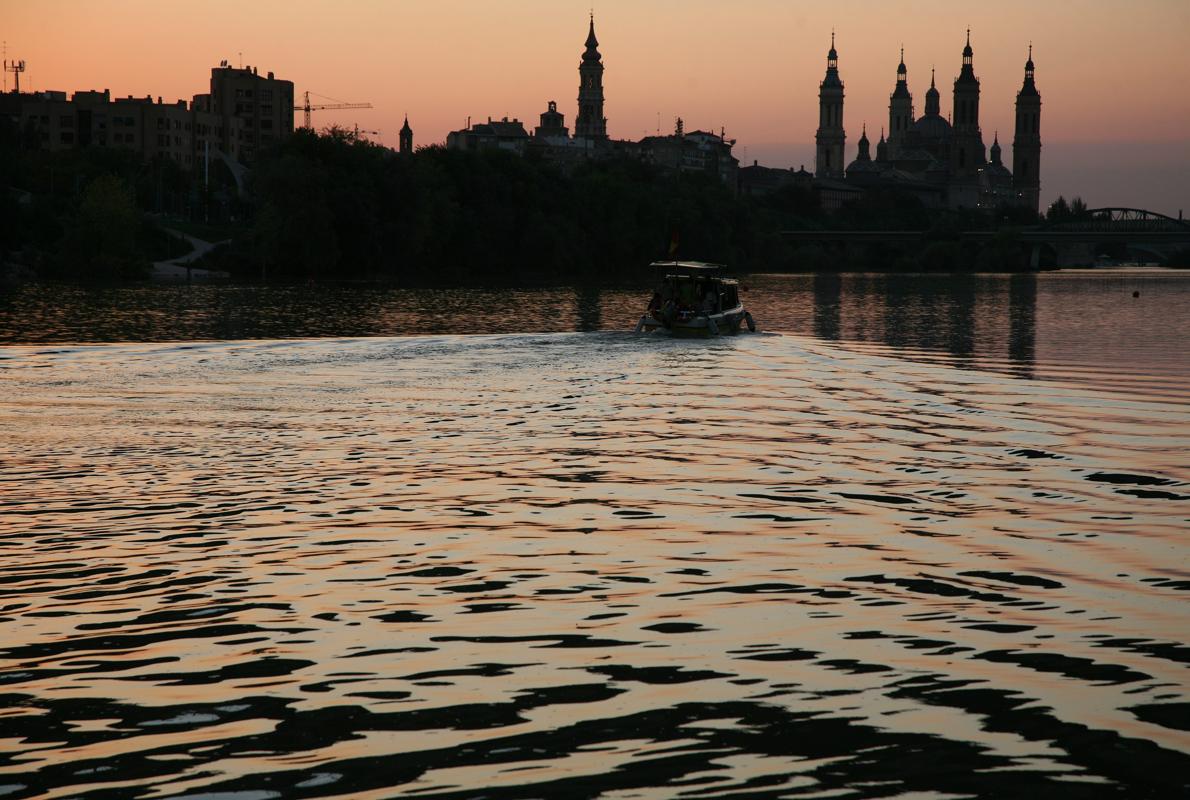 Barco turístico surcando las aguas del Ebro al atardecer, con la Basílica del Pilar de fondo