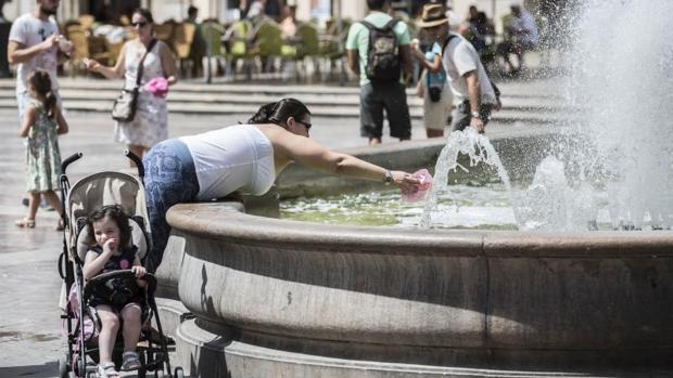 Una mujer se refresca en la fuente de la plaza de la Virgen