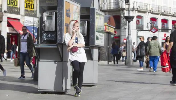 Una joven habla por el teléfono móvil, apoyada en una cabina de la Puerta del Sol