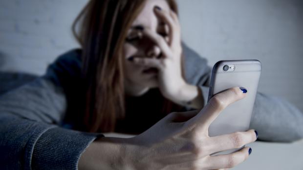 Una adolescente observa, atemorizada, su teléfono móvil