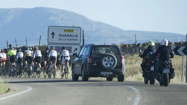 Un grupo de ciclistas circula por Guadalix de la Sierra, seguido de varios vehículos