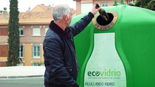 Un hombre deposita una botella de viidrio en el contenedor verde