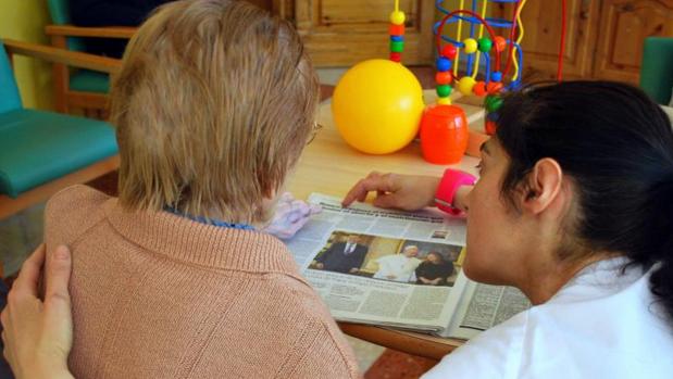 Una cuidadora ayuda a leer el periódico a una mujer dependiente