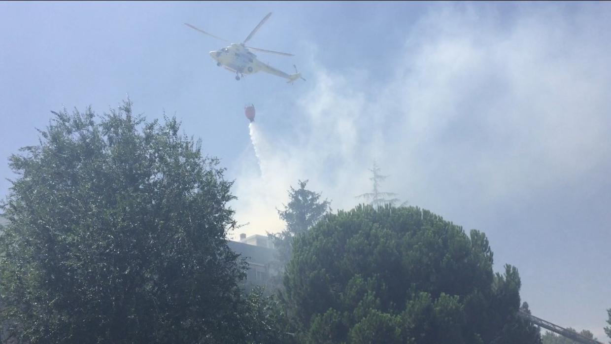 Un helicóptero arroja agua sobre uno de los tejados afectados en Las Rozas