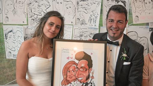 Una pareja muestra su caricatura delante de un mural con los retratos de los invitados