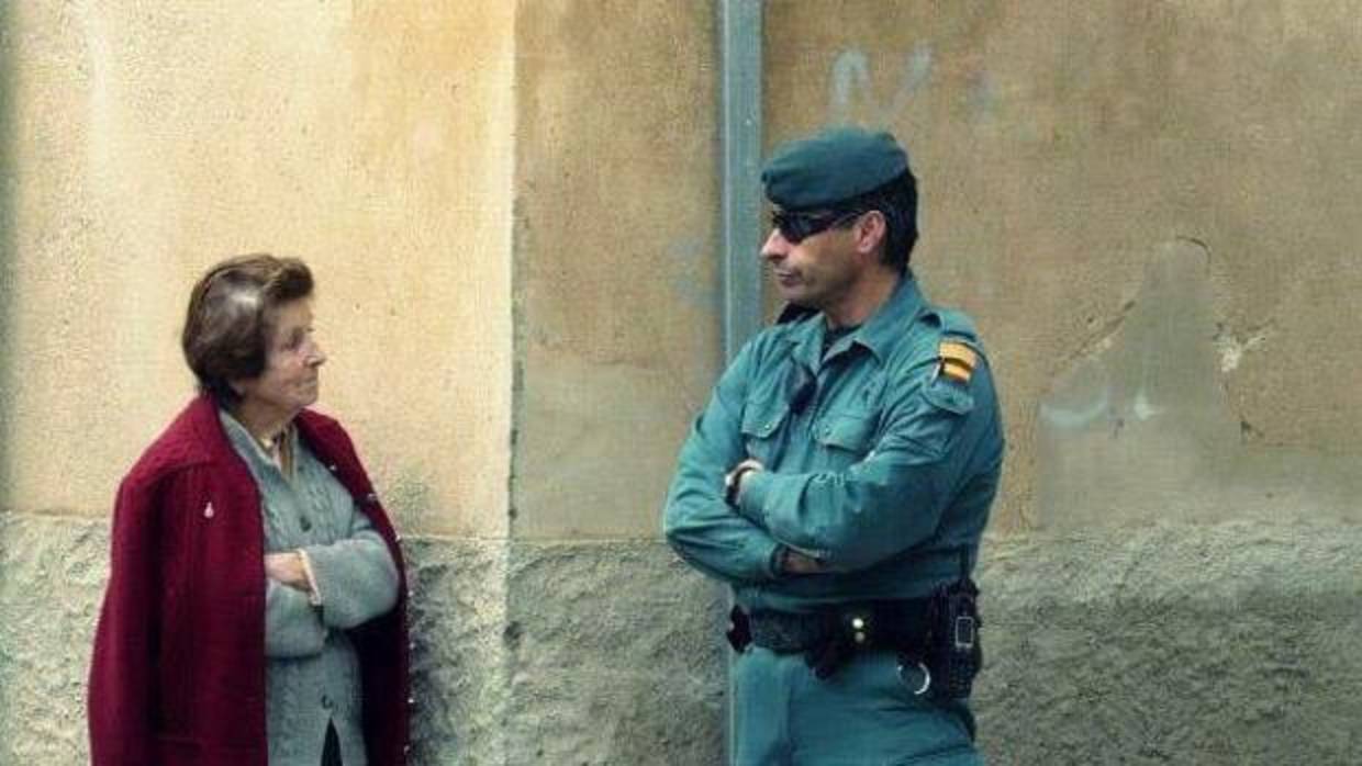 En la fotografía originaria, tomada el 27 de enero de 2012, una señora espera ante un guardia civil a que concluya el dispositivo de seguridad montado aquel día en la Plaza de la Constitución de Felanitx para poder volver a su casa