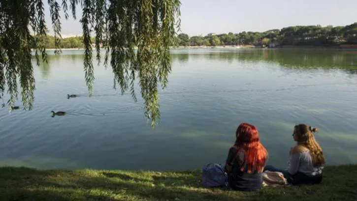 Dos jóvenes se sientan sobre la zona del lago de la Casa de Campo que se convertirá en una «playa»