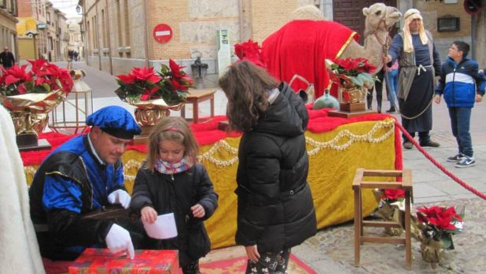 El paje indica a una niña por dónde introducir su carta a los Reyes Magos en una caja, mientras que el camello posa para las fotografías