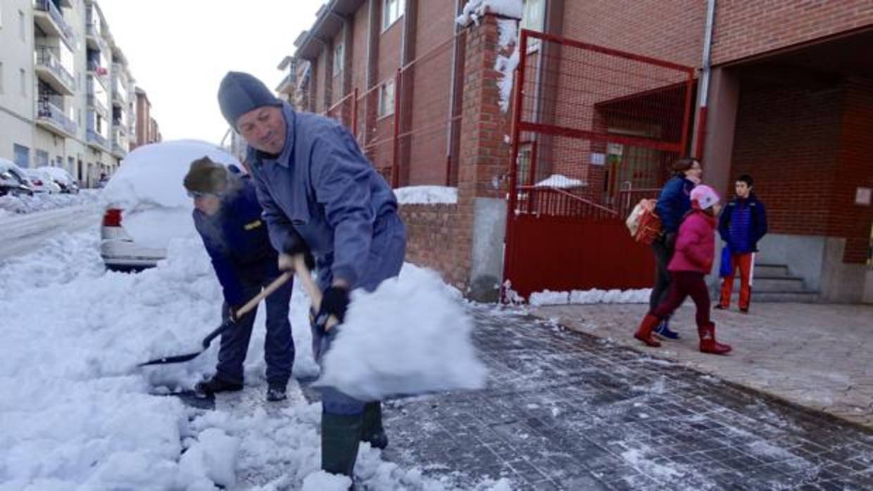 Dos operarios tratan de quitar la nieve a las puertas de un colegio, en la capital abulense
