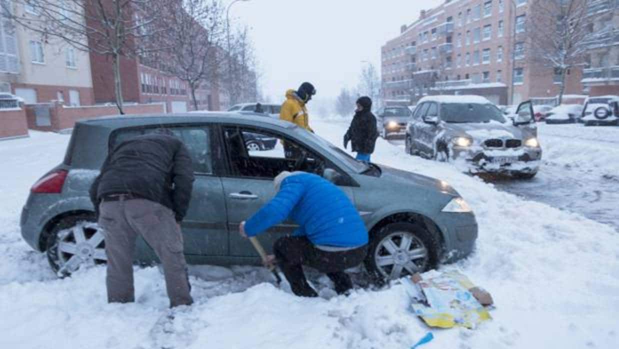 Vecinos abulenses intentan quitar la nieve caída alrededor de su coche