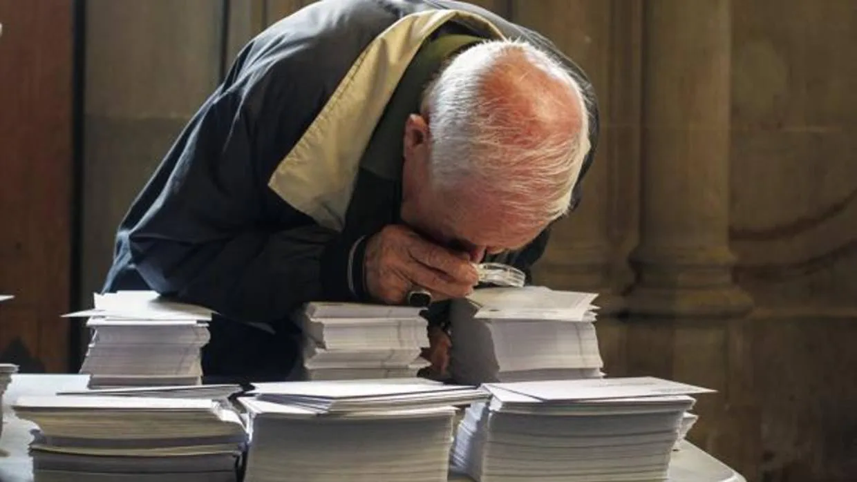 Un ciudadano revisando con una lupa papeletas electorales de distintos partidos