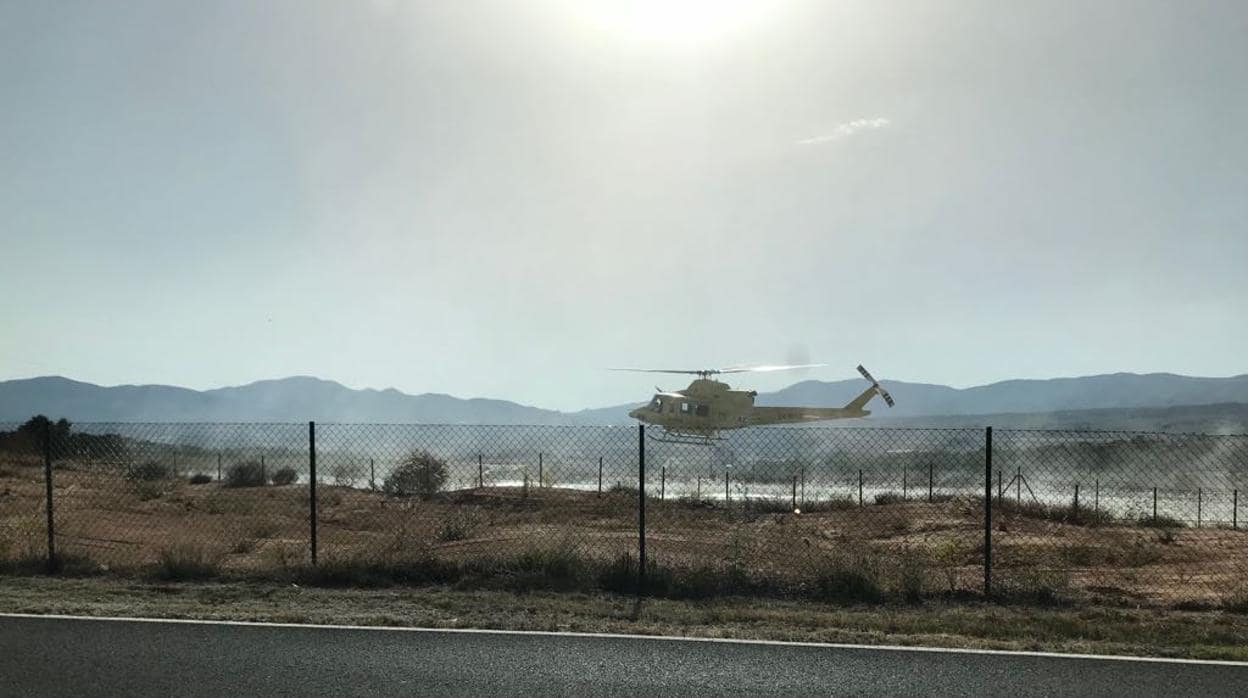 Un helicóptero carga agua en un depósito de agua a cielo abierto próximo a la zona del fuego