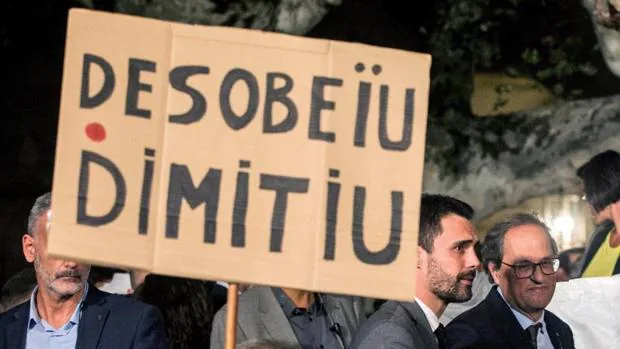 Roger Torrent y Quim Torra, este lunes en la manifestación a las puertas del Parlamento catalán, pasando al lado de un cartel que les exige la desobediencia a las leyes o la dimisión de los cargos públicos