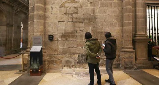 Dos turistas contemplan una puerta tapiada, al descubierto tras la retirada de un confesionario