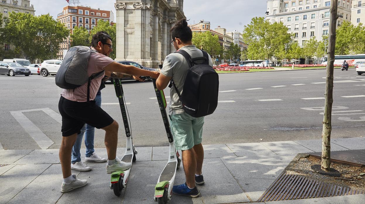 Dos jóvenes cogen dos patinetes de la compañía Lime, frente a la Puerta de Alcalá