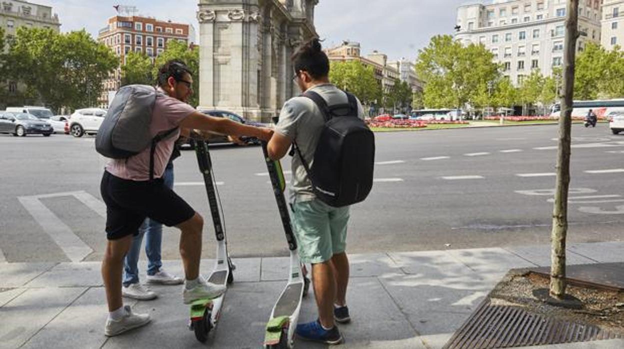 Dos jóvenes cogen dos patinetes de la compañía Lime, frente a la Puerta de Alcalá