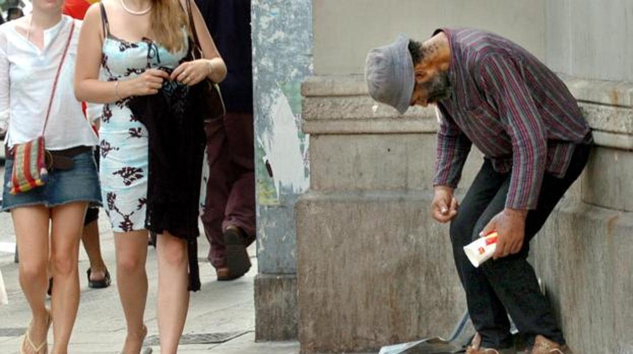 Varias personas pasan junto a un mendigo en Barcelona.